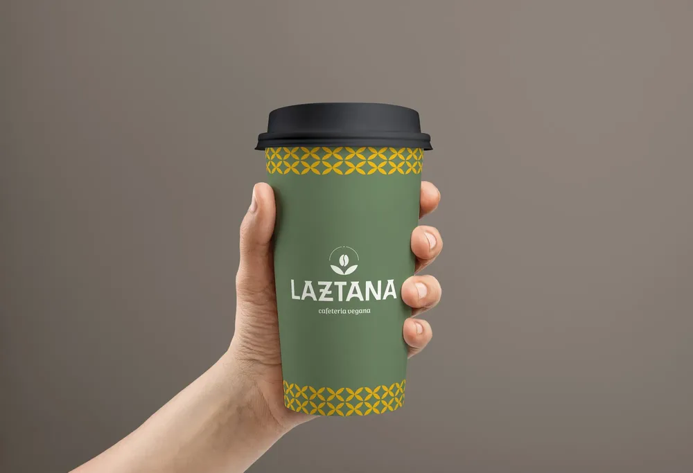 Vaso sujetado por una mano con el logo de una cafetería vegana Laztana en Bilbao.